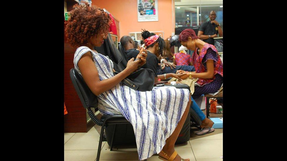 A customer reading her phone at Bruno's Place hair salon in Ikeja Mall in Lagos, Nigeria