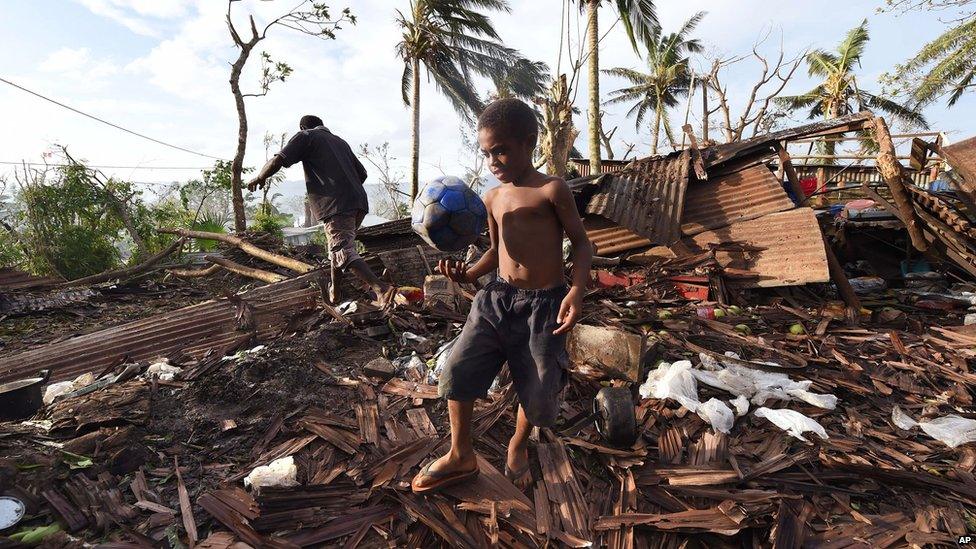 Samuel, only his first name given, carries a ball through the ruins of their family home as his father, Phillip, at back, picks through the debris in Port Vila, Vanuatu in the aftermath of Cyclone Pam Monday, 16 March 2015.