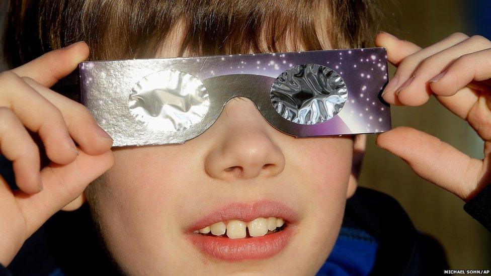 A boy poses for a photograph and looks up to the sun wearing protective goggles in Berlin, Germany