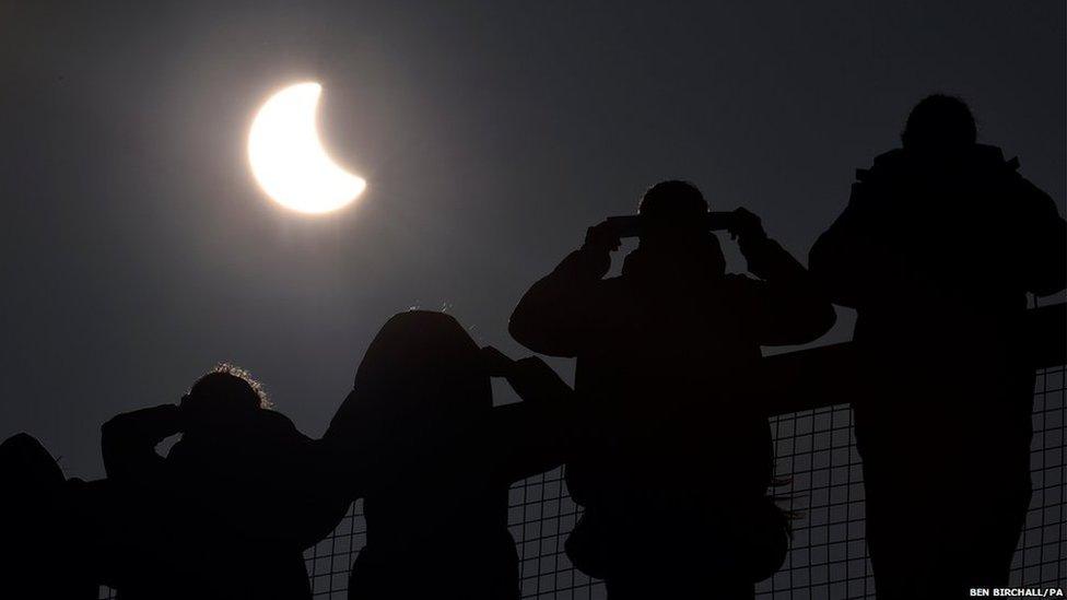 People watch as an eclipse of the sun begins over the Eden Project