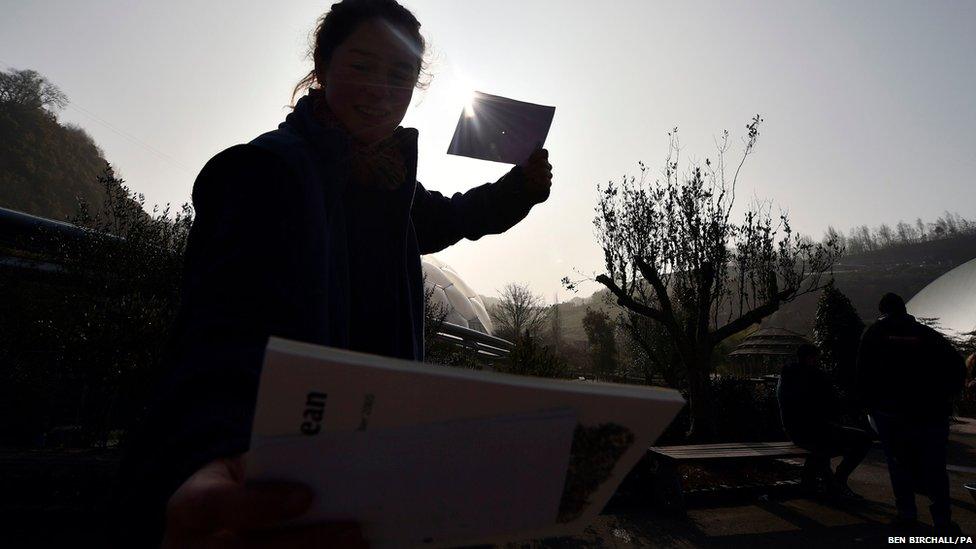 A woman watches the eclipse of the sun through pinhole camera at the Eden Project