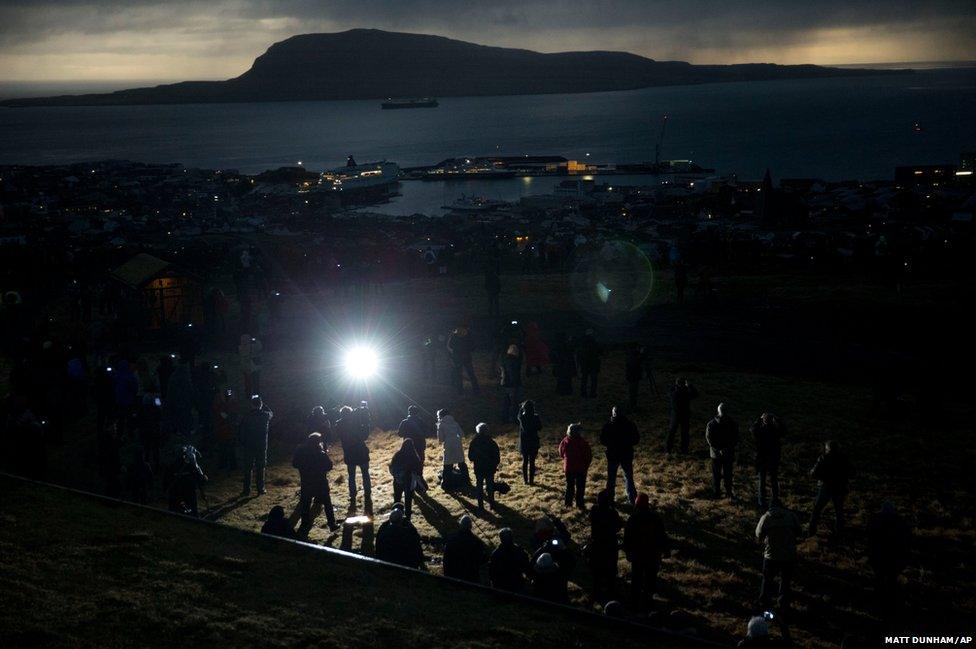 People watch in darkness during the totality of a solar eclipse in Torshavn in the Faroe Islands