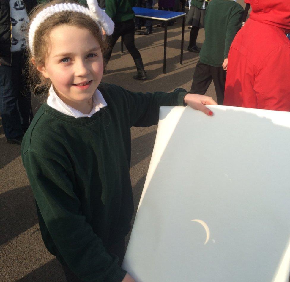 A girl holds up a board with a projection of the eclipse on it