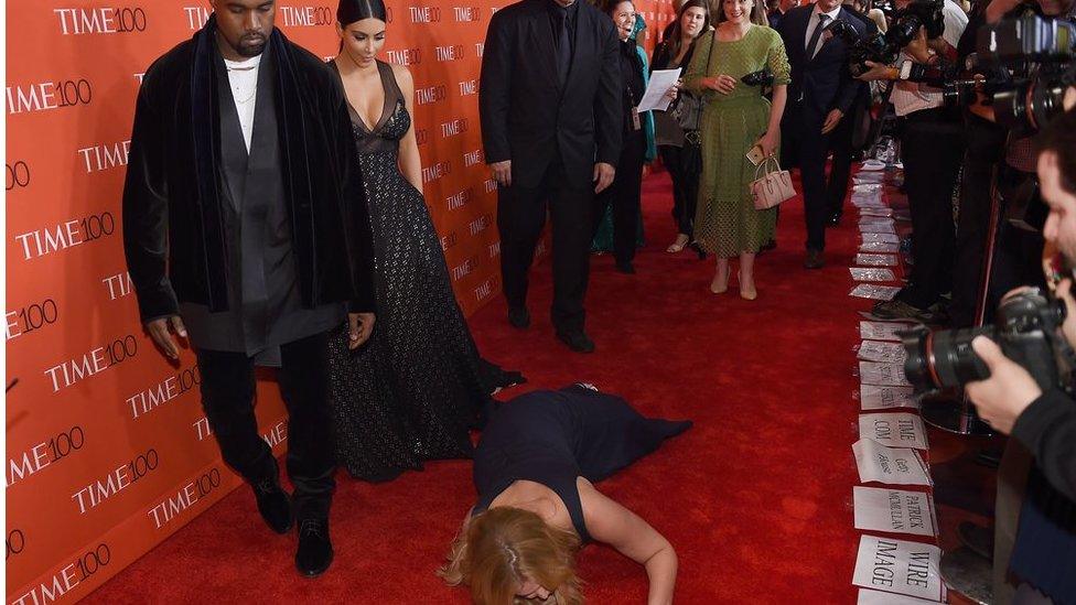 Comedian Amy Schumer pretends to trip and fall on the floor in front of Kim Kardashian and Kanye West