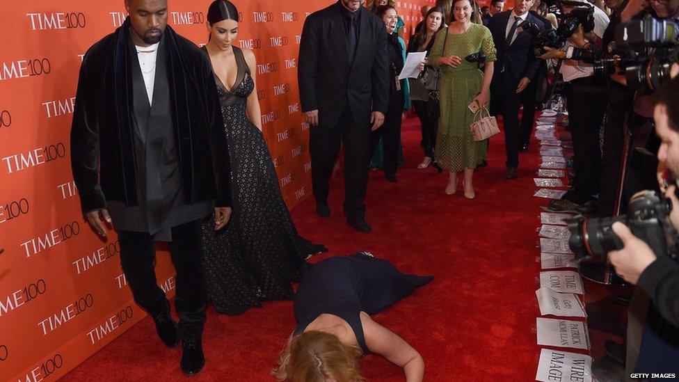 Comedian Amy Schumer pretends to trip and fall on the floor in front of Kim Kardashian and Kanye West