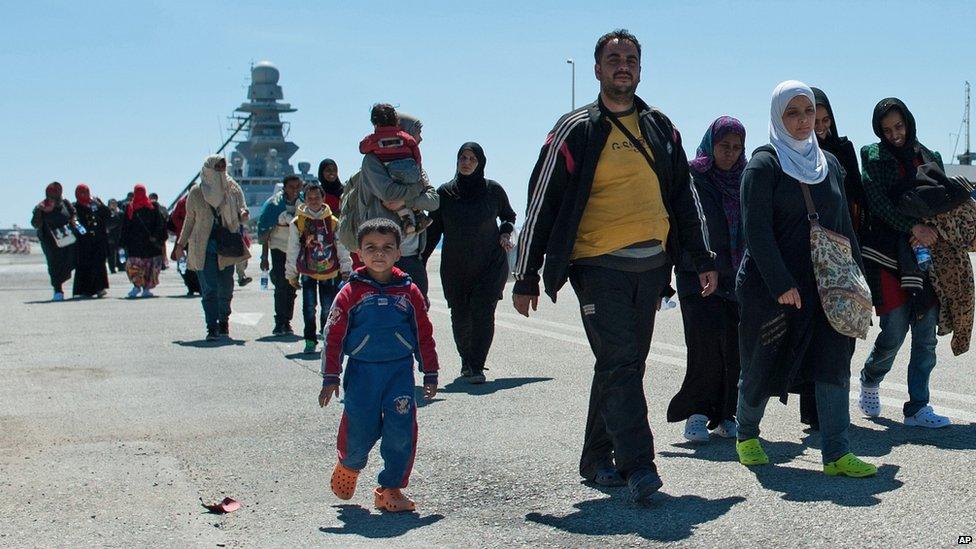 Rescued migrants walk after disembarking from the Italian Navy vessel Bettica in the harbour of Augusta, Sicily