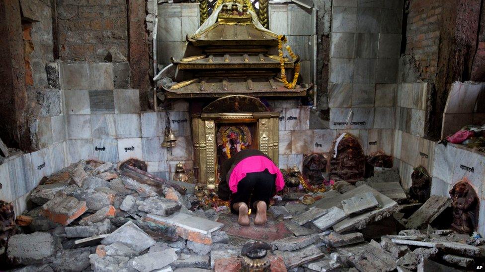 A woman prays at a shrine in a destroyed temple