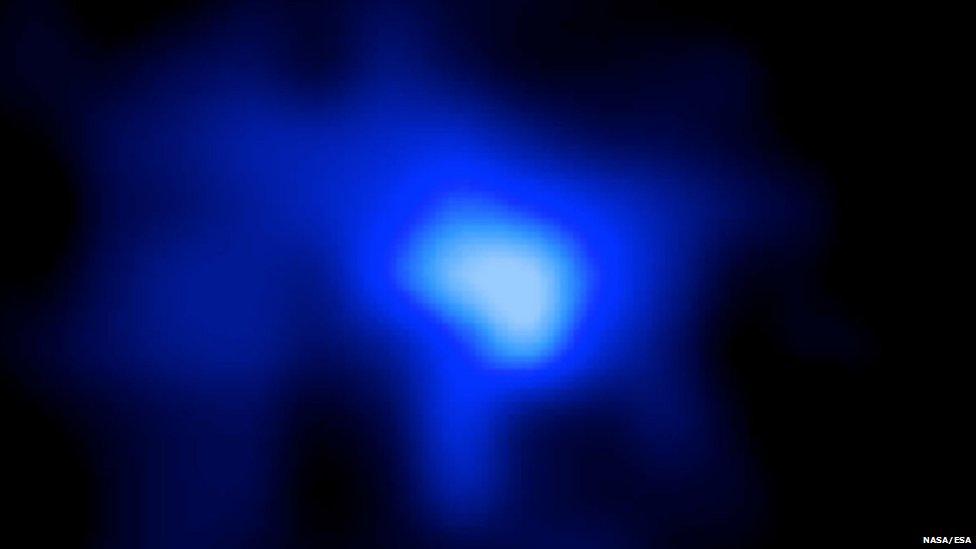 An image of a far away galaxy captured by astronomers. The galaxy appears as a bright blue flare against the blackness of space.