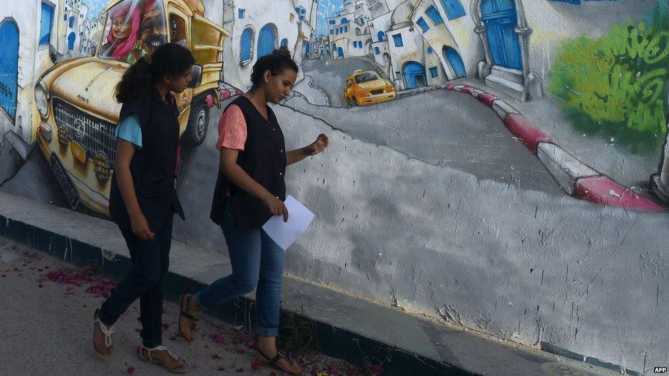 Tunisian girls walk passed a wall covered in graffiti near the Ghriba Synagogue on 5 May 2015 on the eve of the annual Jewish pilgrimage to the synagogue on the Mediterranean resort island of Djerba