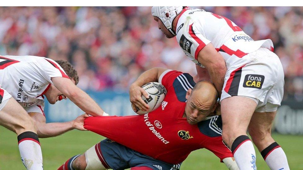 Munster prop BJ Botha is brought to ground by Rory Best and Darren Cave