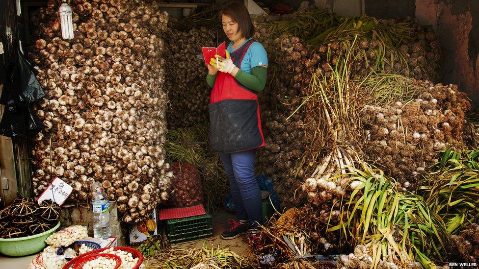 A garlic seller checks her mobile phone at Gupo market.