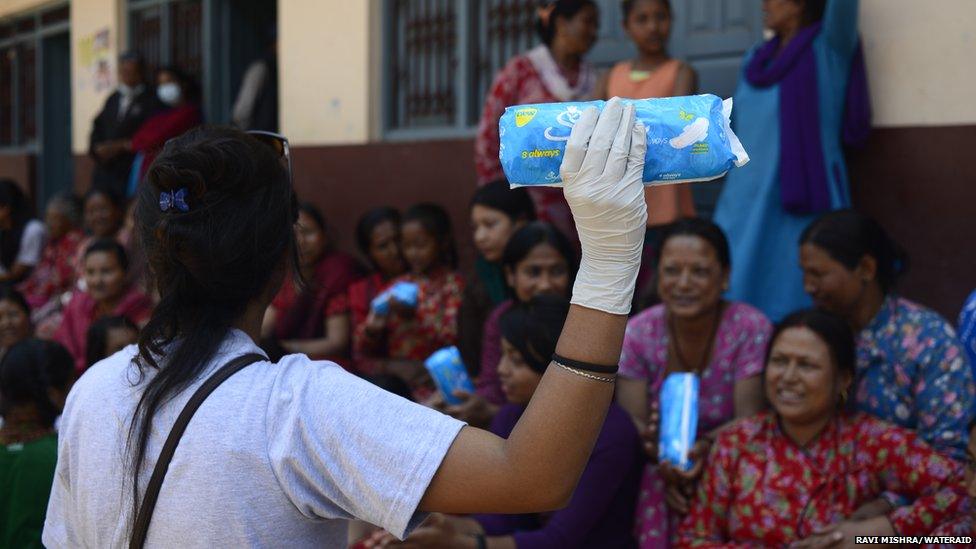 Woman holding a packet of sanitary towels while giving a talk to other women