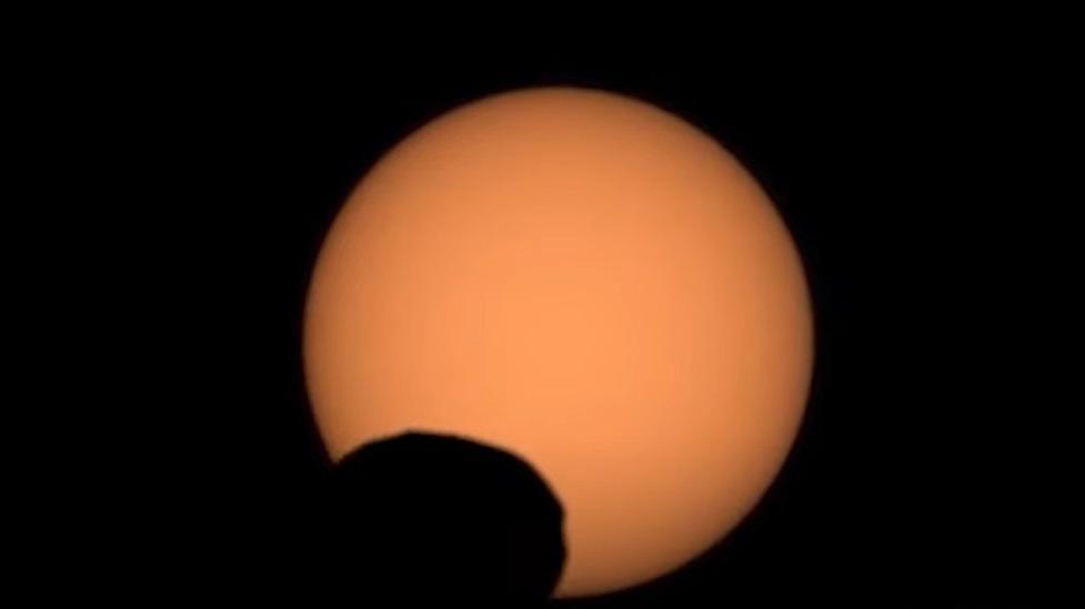 The sun with silhouette of Phobos on surface