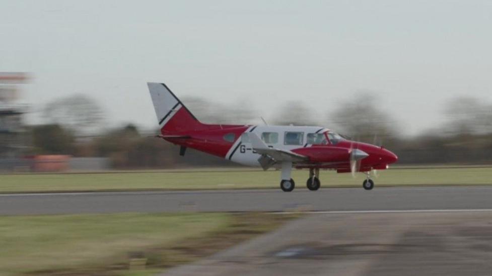 A picture of a red and white light aircraft landing on a runway. 