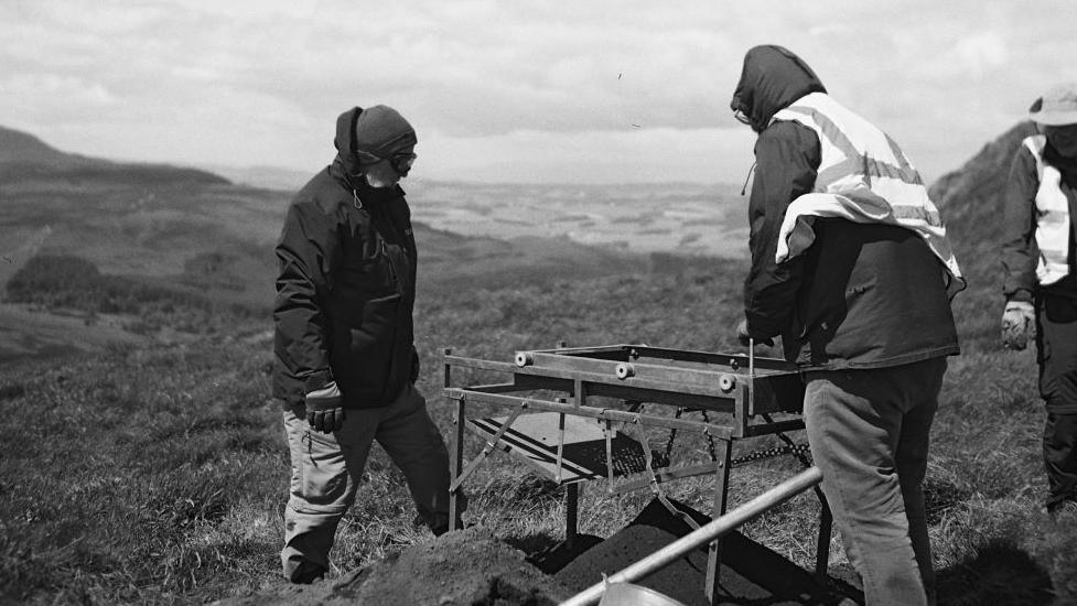 Archaeologists using a tool to sieve soil to find artefacts on East Lomond hill. 