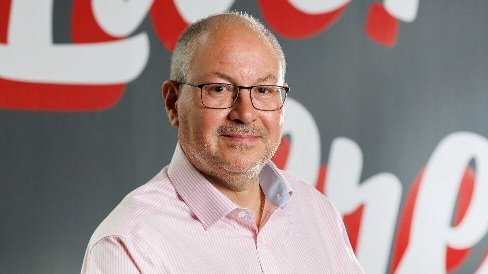 Luke Farajallah in a pink shit and glasses, bald with short grey hair at sides, head and shoulders shot, with slight smile for camera.