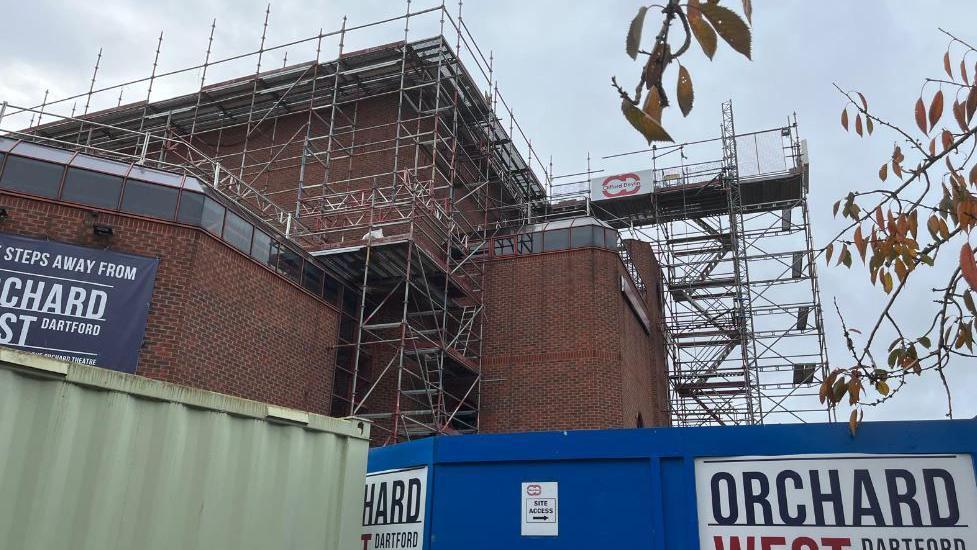 Exterior shot of Orchard theatre covered in scaffolding with tree branches in foreground