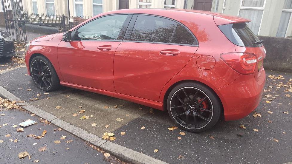 A red car parked on a pavement in a residential area. 