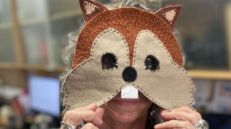 A staff member at Acorn is holding up a home made fabric face mask of a red squirrel to wear for the event.