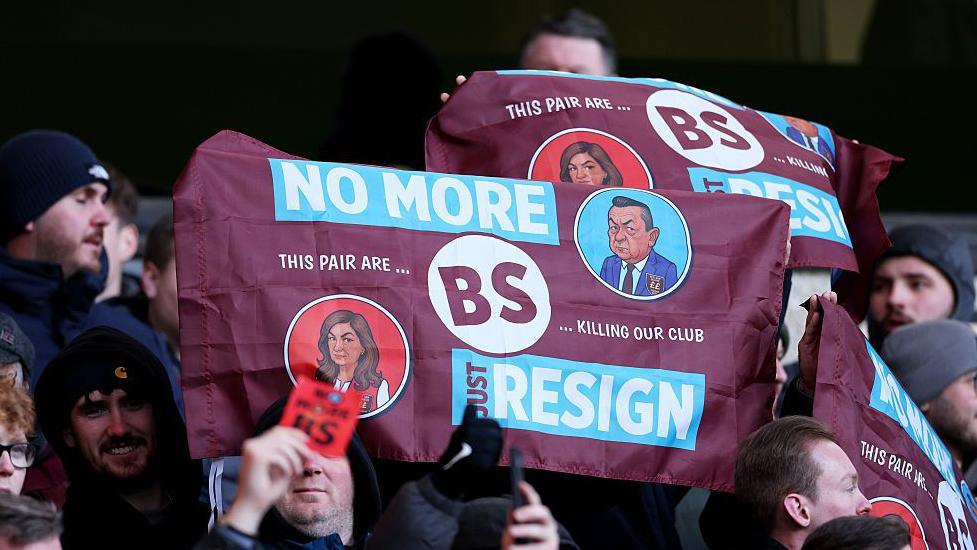 A claret and blue banner with "No more BS. Just resign" in big capital letters and "this pair are killing our club" emblazoned on it, held by West Ham fans as they protest against Karren Brady and David Sullivan