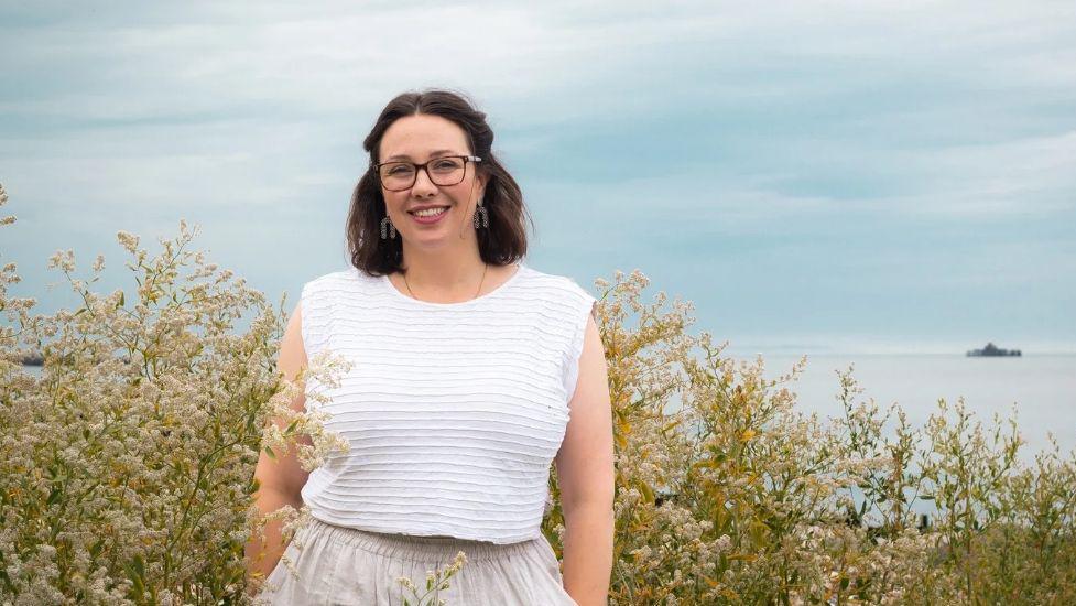 Sam Kennedy Christian wearing a white textured sleeveless top and linen trousers standing in front of a view of the sea in Herne Bay