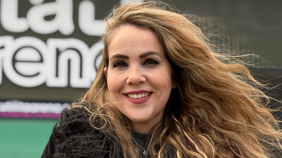 A woman with dark blonde hair wearing a black fluffy jacket stands in front of the arena entrance.