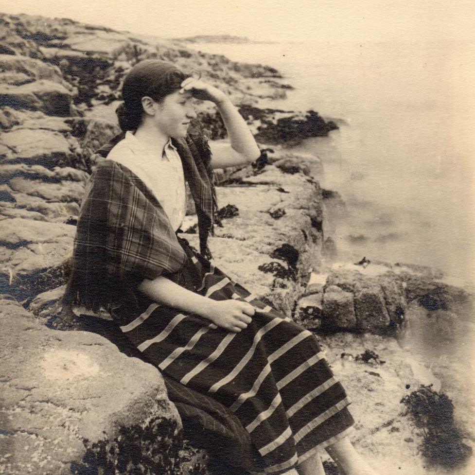 A woman shading her eyes with a hand as she looks out to sea