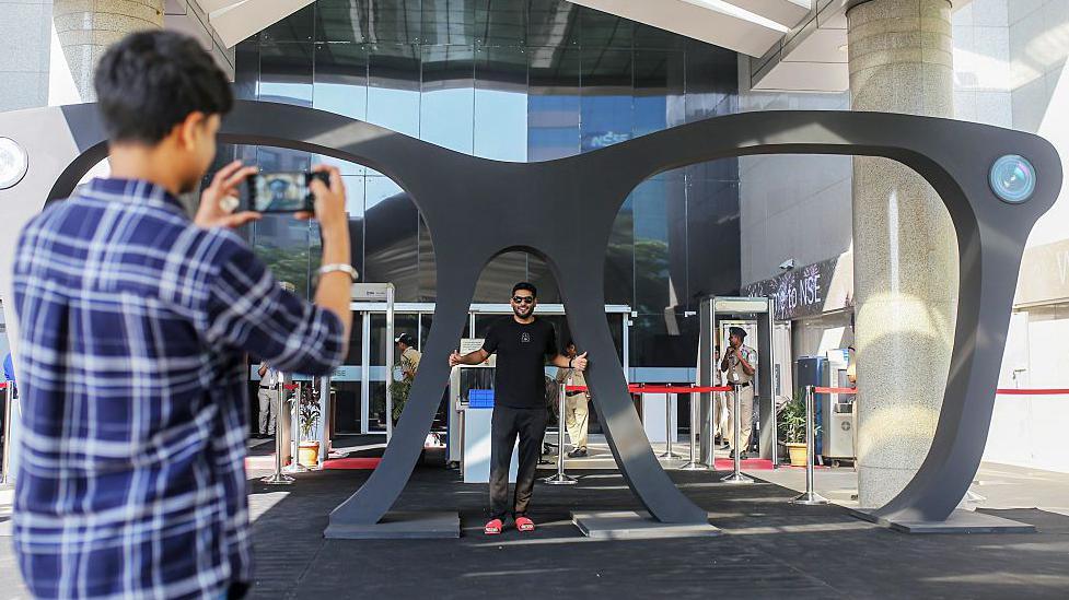 An attendee poses for photos with a giant pair of glasses following the Lenskart listing ceremony at the National Stock Exchange (NSE) in Mumbai, India, on Monday, 10 November 2025.