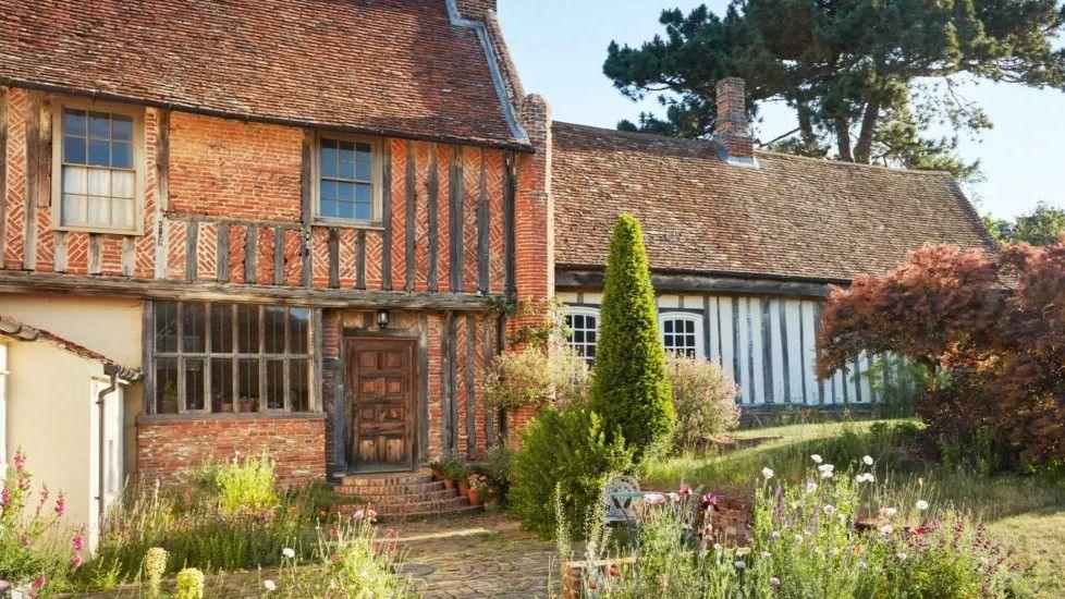 A Tudor home and a garden in front of it. The home is made of red brick and wooden beams.