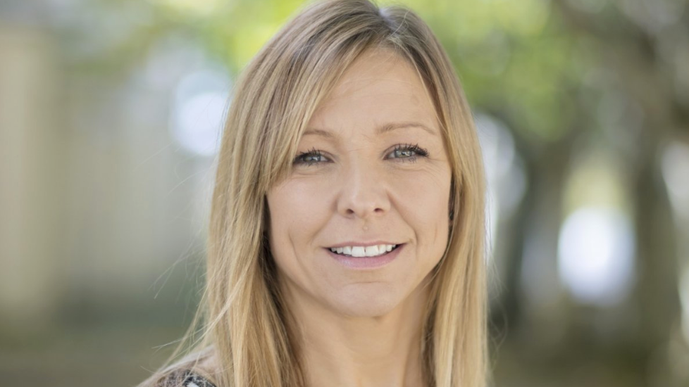 A fair-haired woman with long hair and a defused background.