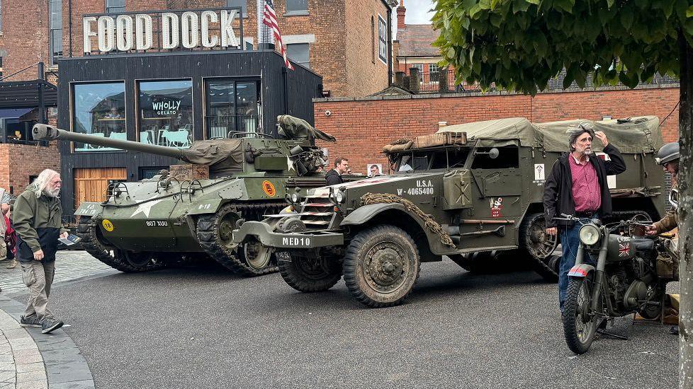 A tank, army 4x4 and army motorbike in a city centre