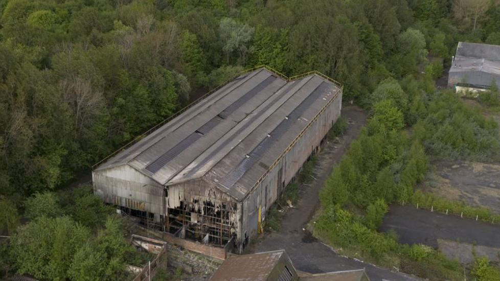 An aerial shot of the building where the fire took place. The front is damaged. It is surrounded by trees.