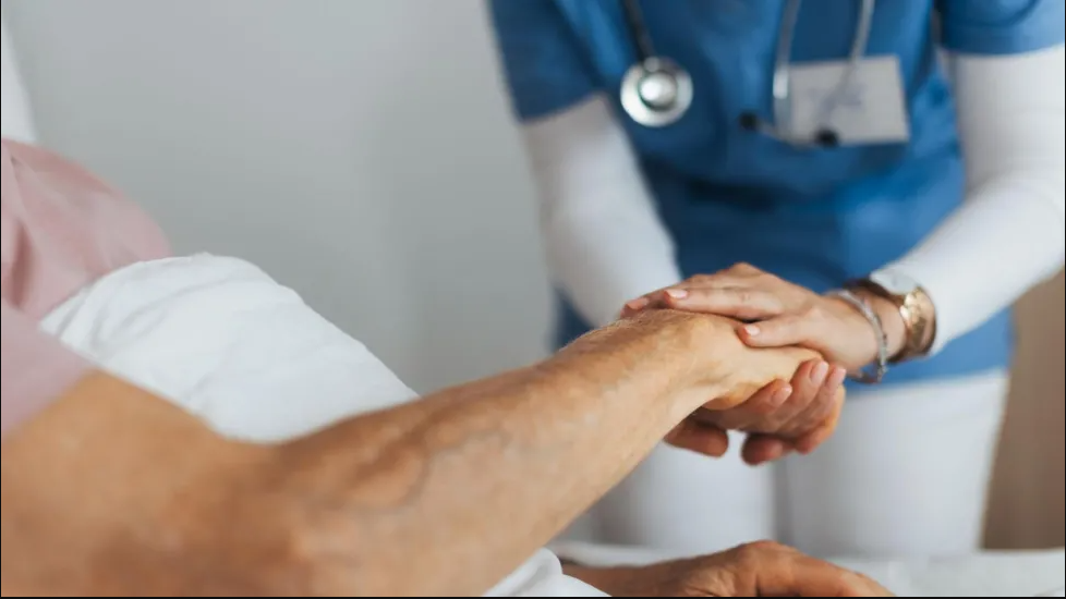 An older person holding hands with a person dressed in medical uniform