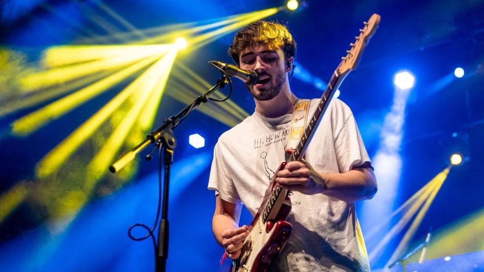 Alfie Templeman on stage with blue and yellow lights behind him