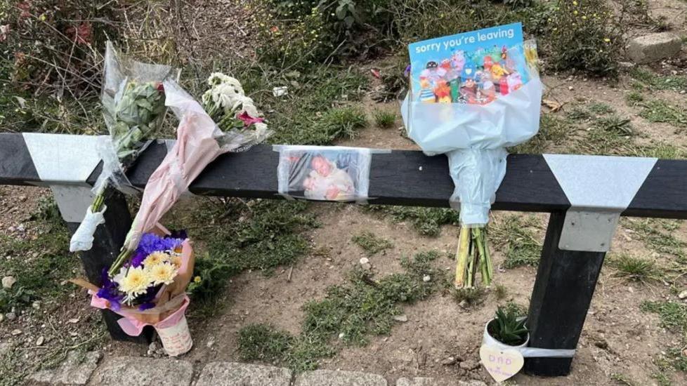 Flowers left by a fence on a street where Gary Hindle was killed. They are taped to a wooden fence. There is a picture of Gary also taped to the fence.