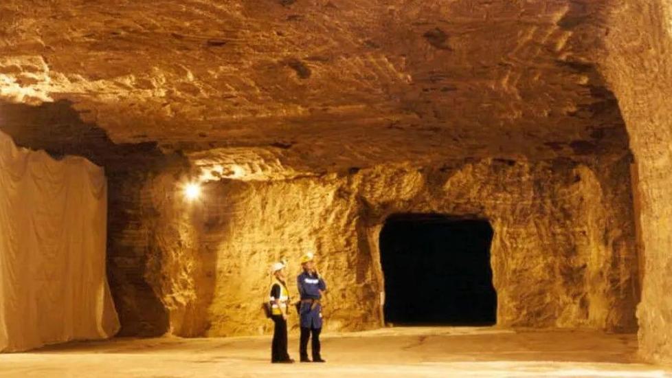 Two people wearing personal protection equipment and hi vis jackets stand inside a vast cavern carved out of salt in Winsford, Cheshire. 