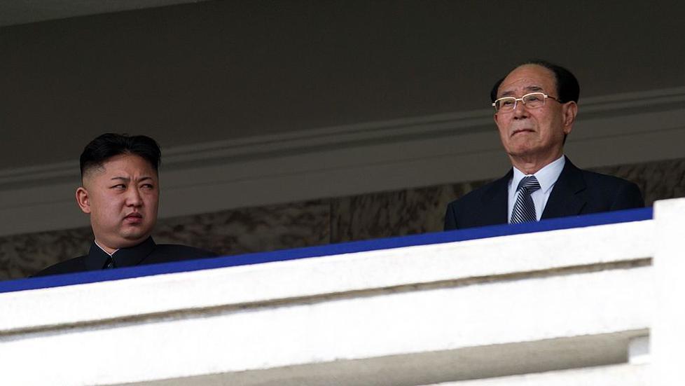 Kim Jong Un standing on a balcony glancing at his side towards Kim Yong Nam