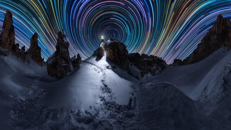 time lapse photo showing snowy landscape with brightly coloured stripes in the night sky