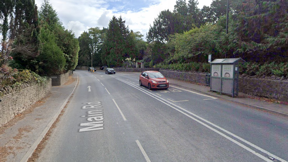 The A370 in Flax Bourton. It is a residential area with a bus stop. There are stone walls on either side of the carriageway and a footpath. 