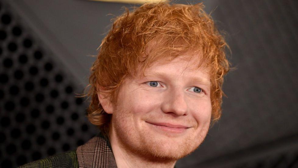 A man with ginger hair is smiling and looking off to the side of the camera.