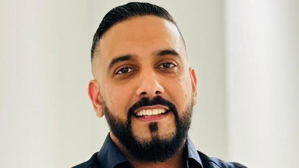 Gurvinder Johal, with dark hair and a beard, smiles.