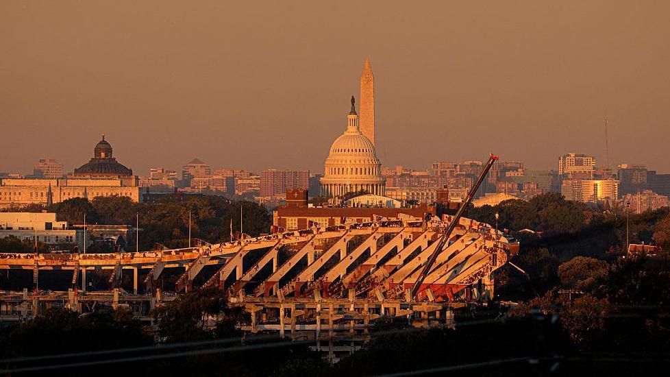 Aerial shot of deconstructed stadium, showing internal beams, with the US Capitol in the background