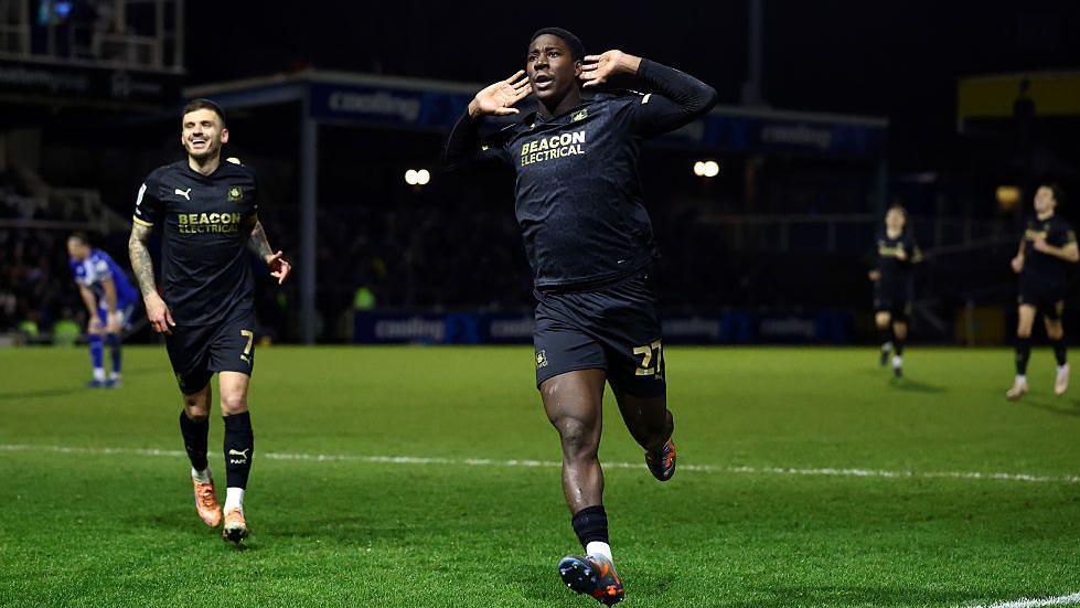 Plymouth Argyle's Aribim Pepple cups his hands to his ears as he runs to the fans to celebrate his match-winning goal.