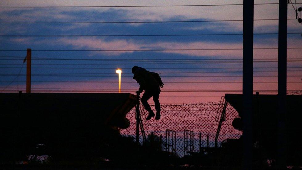 A migrant climbing over a fence on to the tracks near the Eurotunnel site at Coquelles in Calais