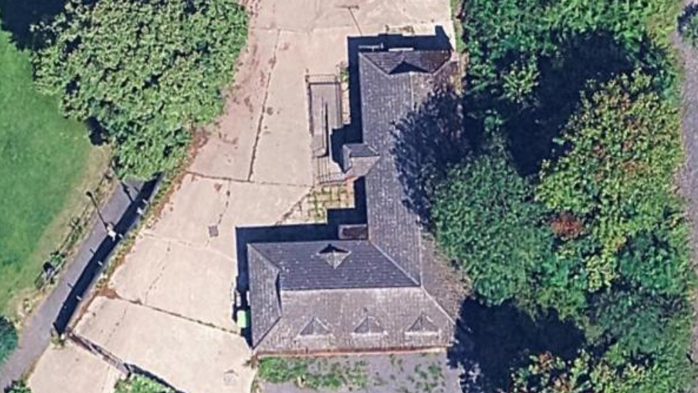 Image from above of an L-shaped building with hardstanding and trees around the building
