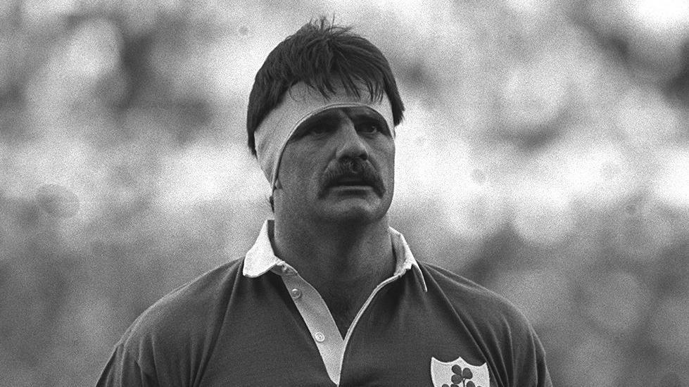 A black and white picture of a man in an Ireland rugby top and bandana round his forehead. 