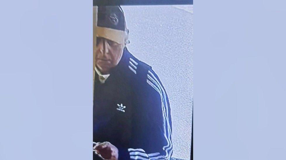 A screengrab from CCTV that shows the man the police want to identify. The photo shows only half of him. He is wearing a baseball hat and a dark-coloured sweatshirt with a white logo on the chest and three white stripes running down his left arm.