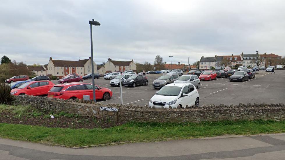 Rock Street Car Park in Thornbury. It is situated on a hill, on a bend in the road. It is surrounded by a brick wall and a pavement.