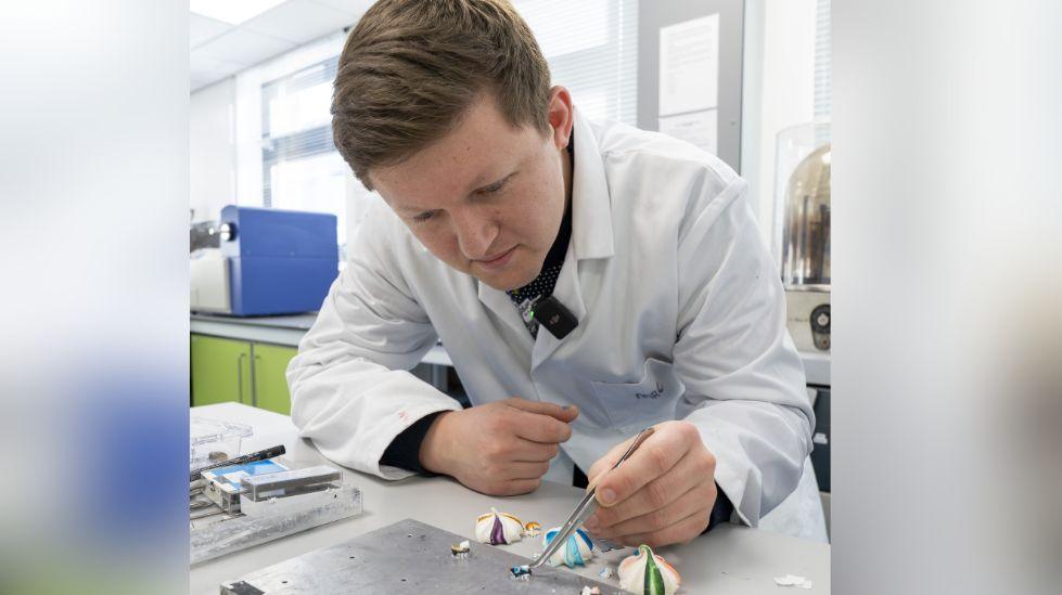 A chemist adding blue icing to the top of a tiny meringue which will go under the microscope