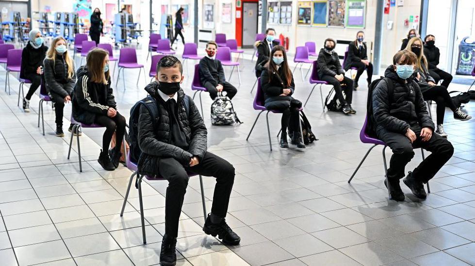 Children sitting in a school hall socially distanced from each other and wearing face masks